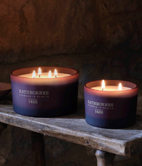 Rathborne's London Candle Collection featuring two scented candles and their packaging on a clean white background. On the left is the '1488' candle in a dark plum glass jar with its purple box.