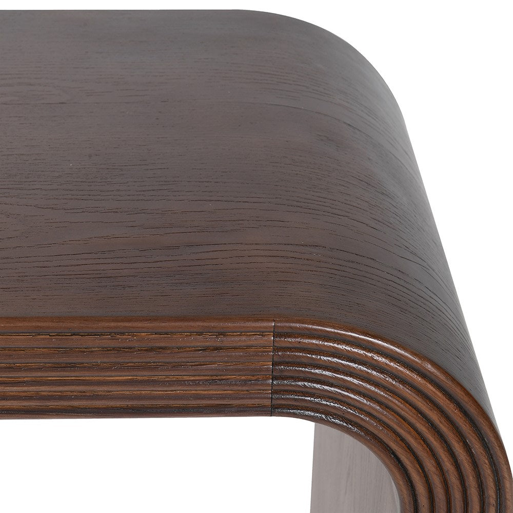 A modern console table with a dark brown wood grain finish, featuring a curved top and thick, blocky legs with concentric grooved detailing, shown on a plain white background.